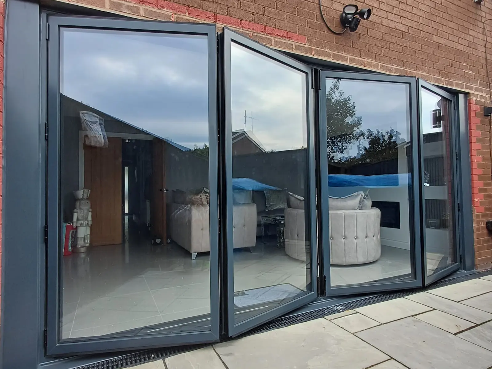 Four-pane anthracite grey aluminium bifold doors open onto a paved patio