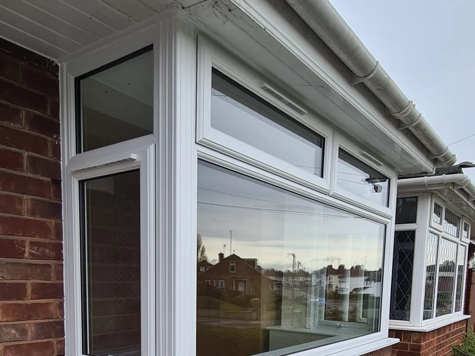 White uPVC square bay window with opening top vents fitted to a red brick bungalow