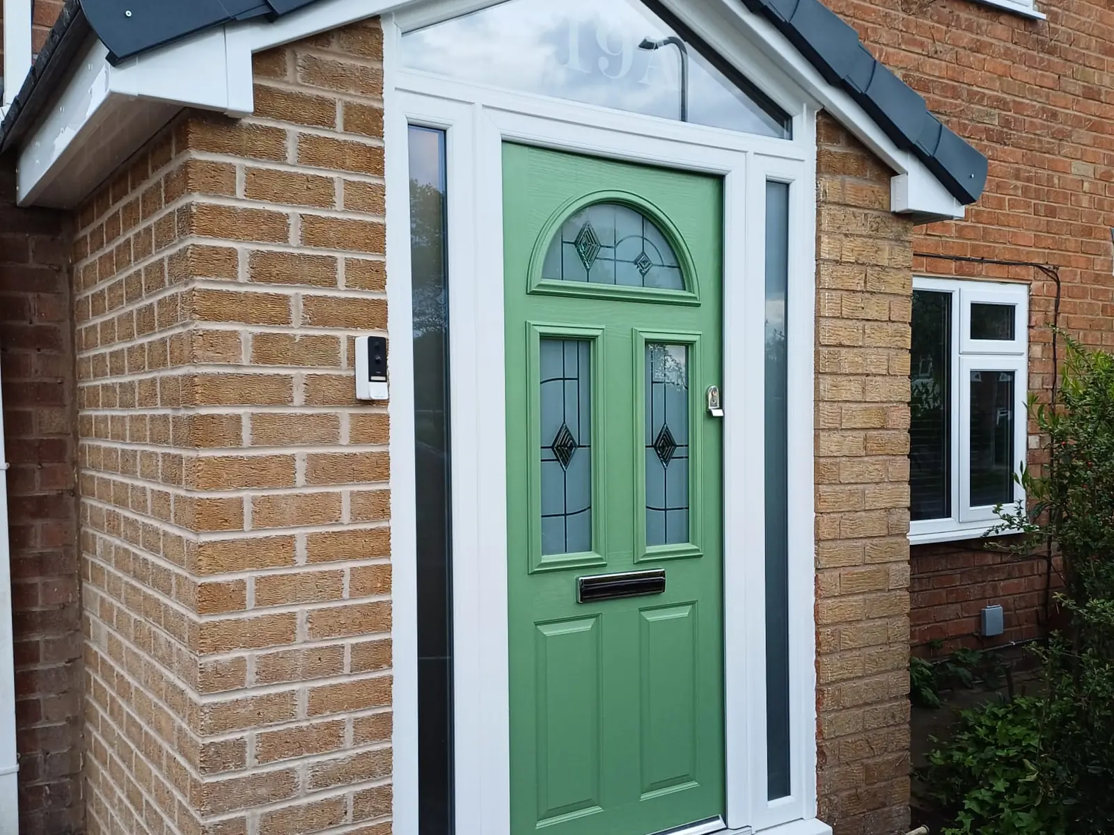 Green composite front door with leaded glass panels, sidelights and a tiled canopy porch