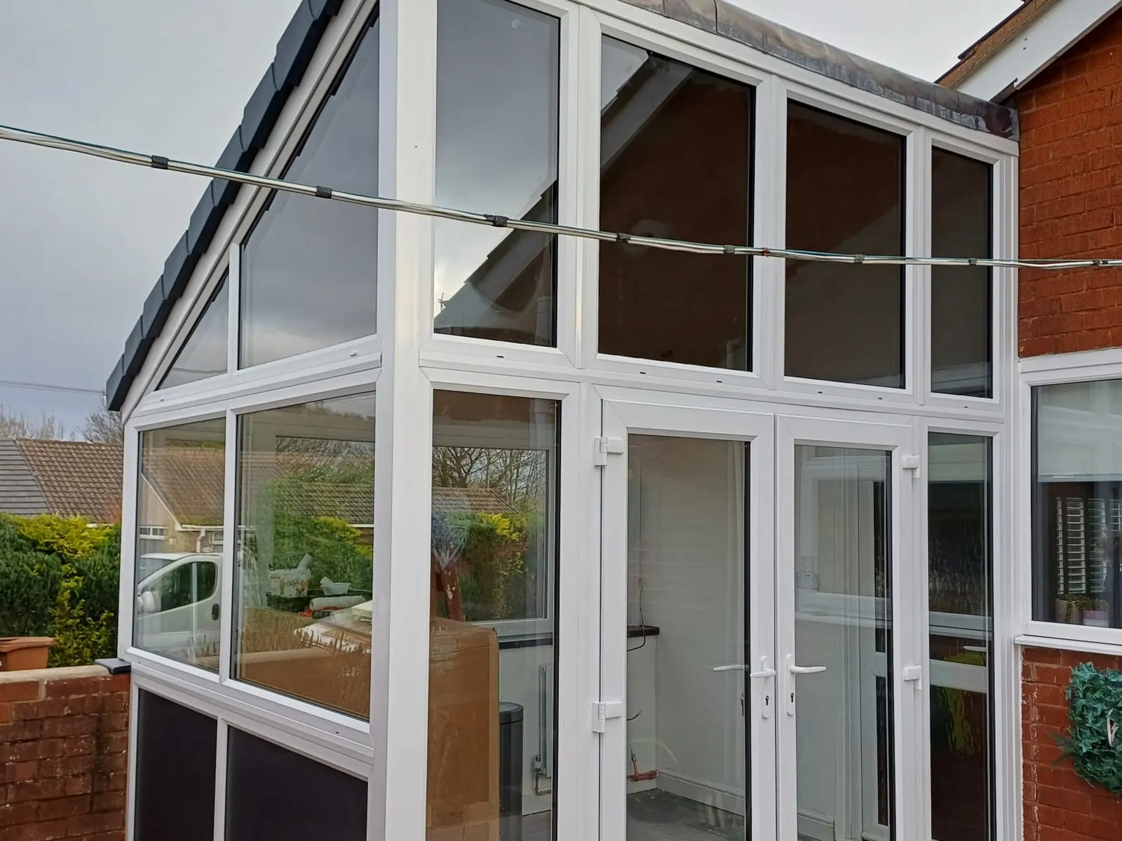 Small white uPVC conservatory with French doors and a tiled solid roof built onto a bungalow