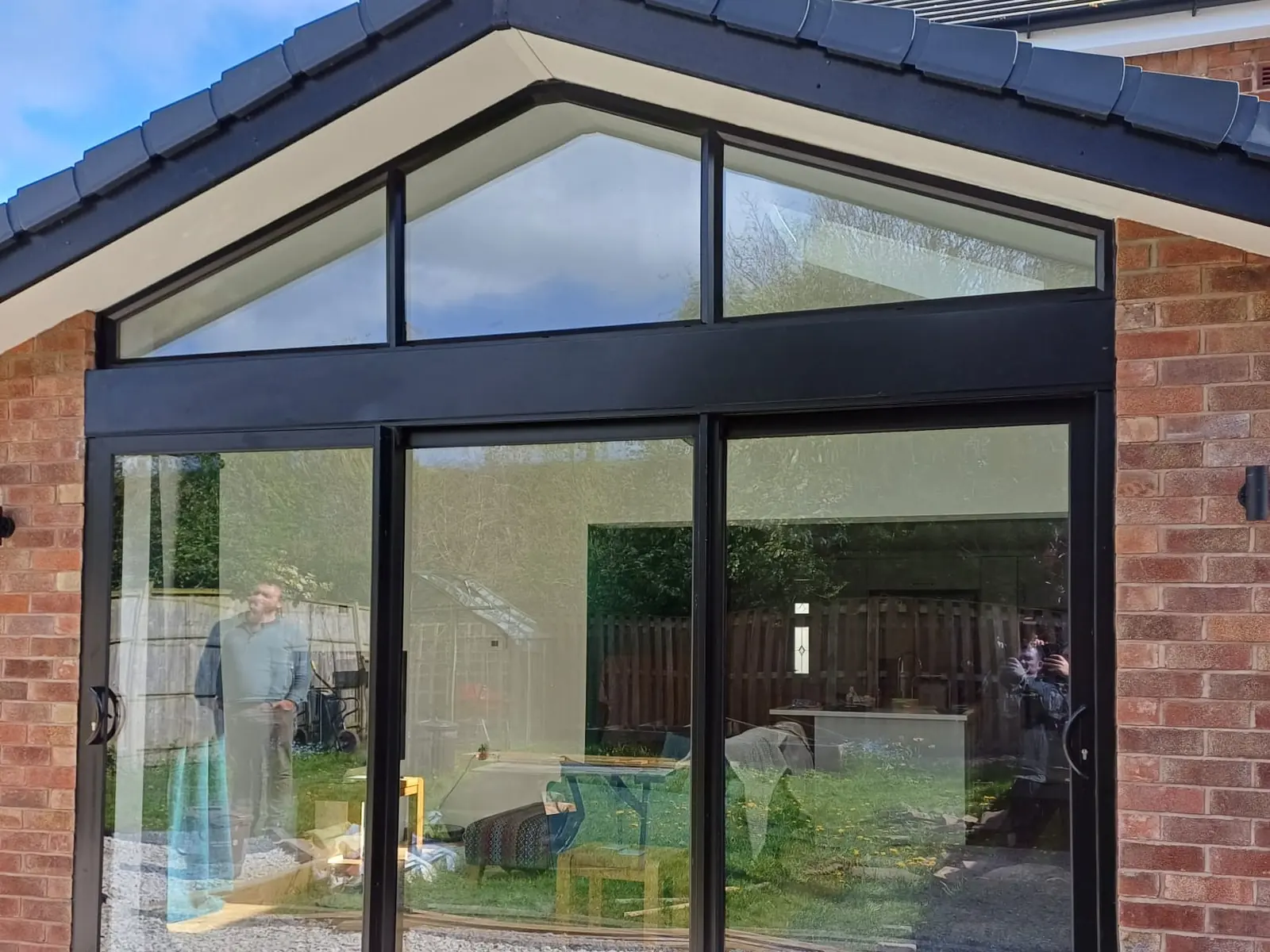 Black aluminium sliding patio doors with a glazed apex above, fitted to a brick bungalow